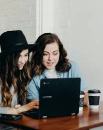 two woman sitting near table using Samsung laptop